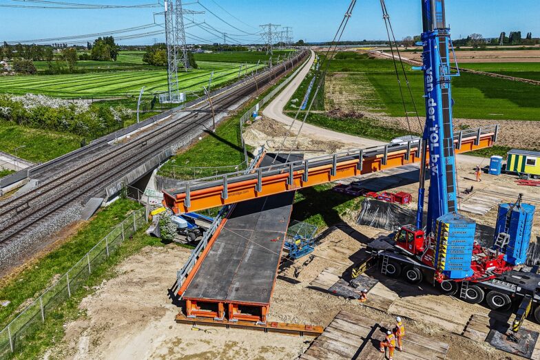 Een luchtfoto van een oranje retrobridge module die op zijn plaats wordt getild door een kraan.