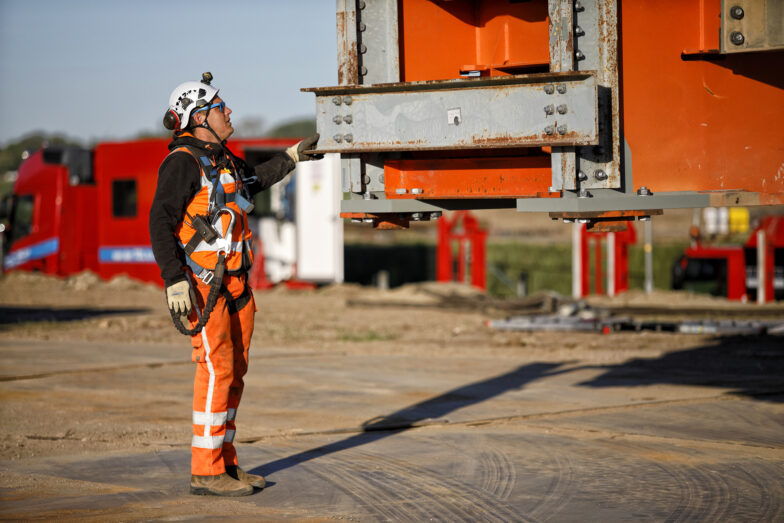 Een arbeider in oranje werkkleding en een helm met gehoorbescherming bekijkt een oranje brugmodule.
